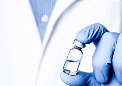 A doctor wearing blue latex gloves holds a glass vial of a liquid biologic drug